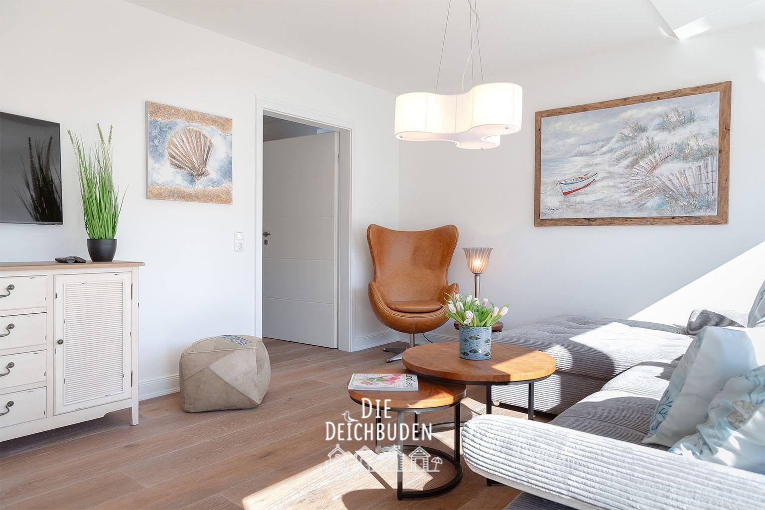 Wohnzimmer mit Sofa, Sessel, Tisch und Wandbildern.