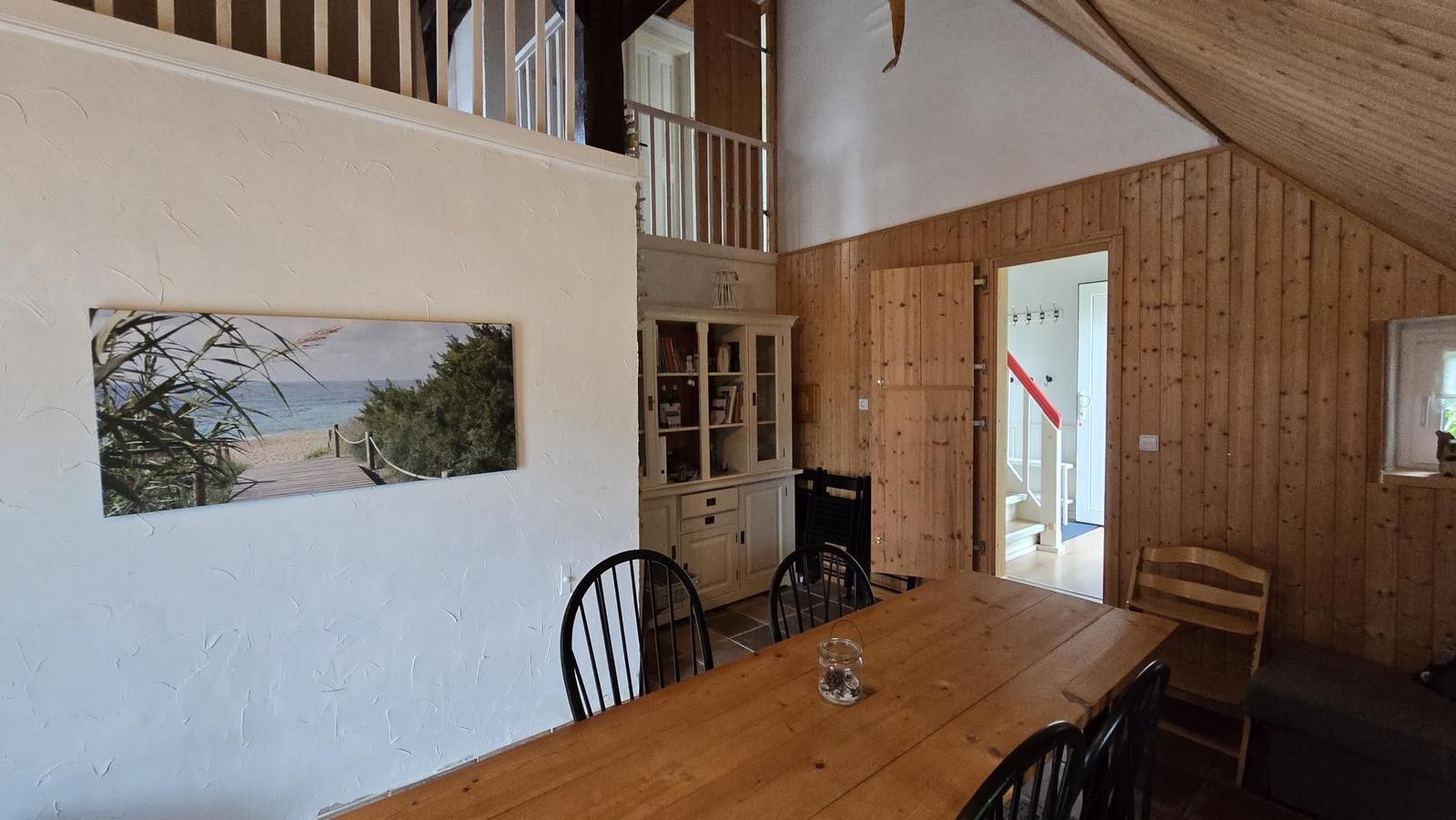 Esszimmer mit Holztisch, Stühlen und Wandbild. Holzwände und Dachschräge.