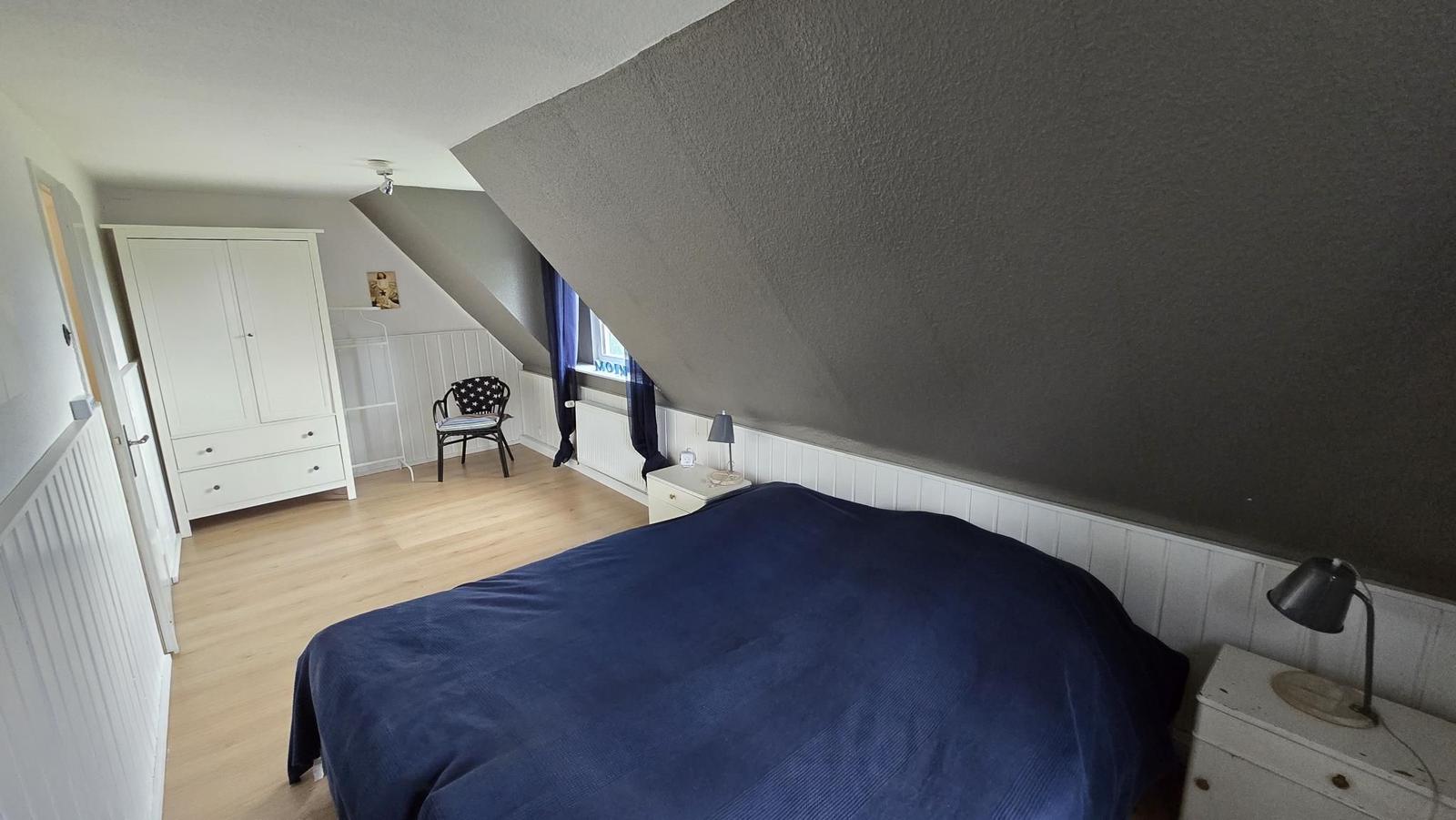 Schlafzimmer mit Dachschrägen, Bett, Kleiderschrank und Stuhl.