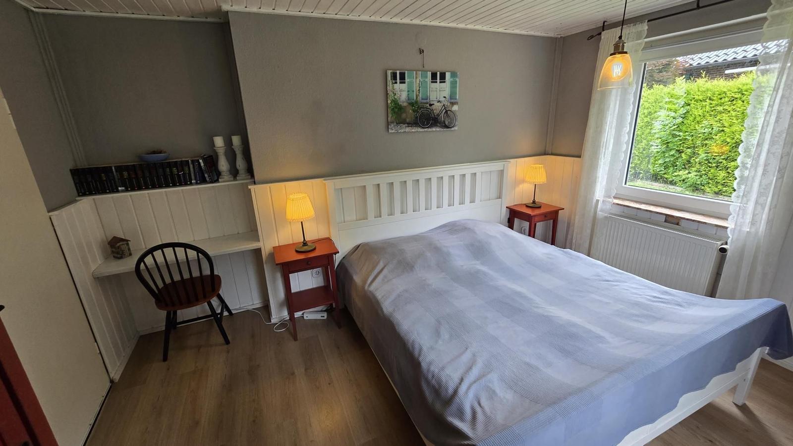 Schlafzimmer mit Bett, Nachttischen und Fenster mit Blick auf Garten.