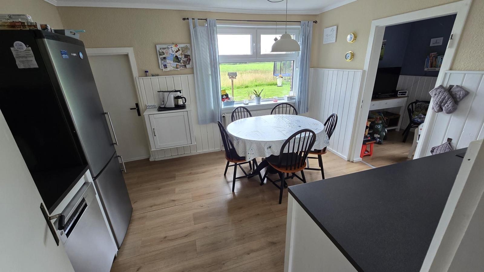 Küche mit Esstisch, Fenster und Blick auf Grünfläche.