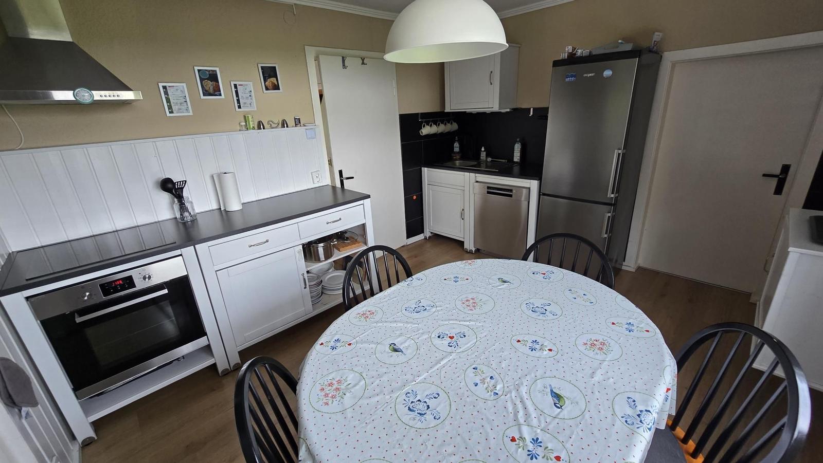 Küche mit Esstisch, Kühlschrank und Herd. Tischdecke mit Blumenmuster.