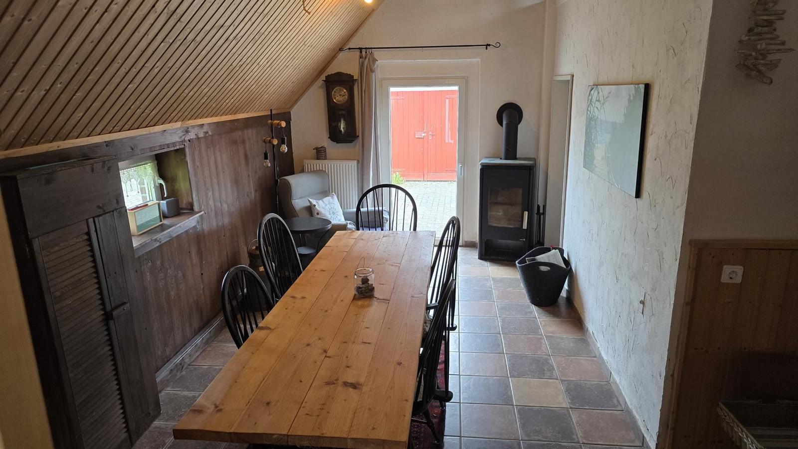 Esszimmer mit Holztisch, Stühlen und Kaminofen. Tür führt nach draußen.