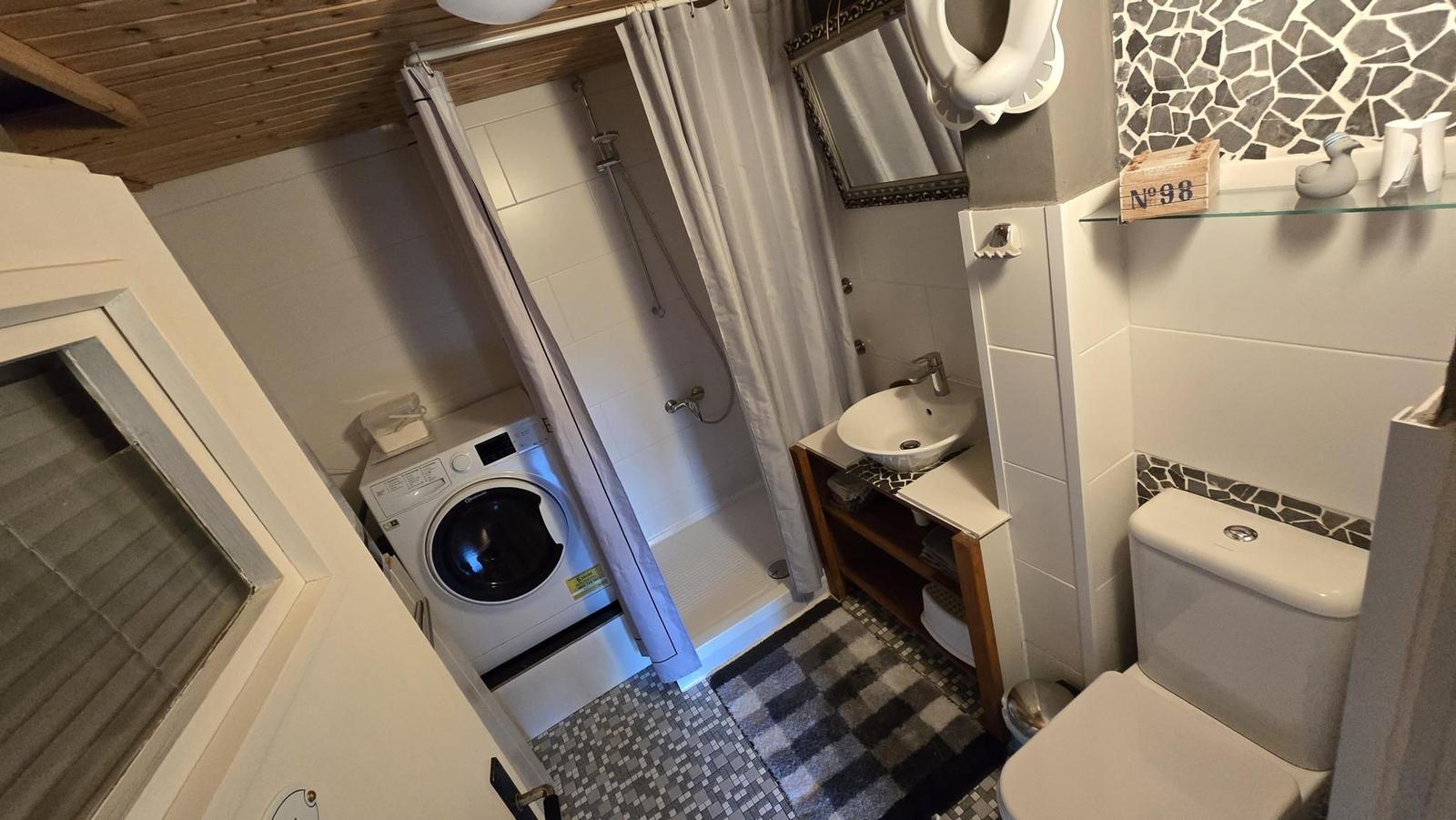 Badezimmer mit Dusche, Waschmaschine, Waschtisch und Toilette.