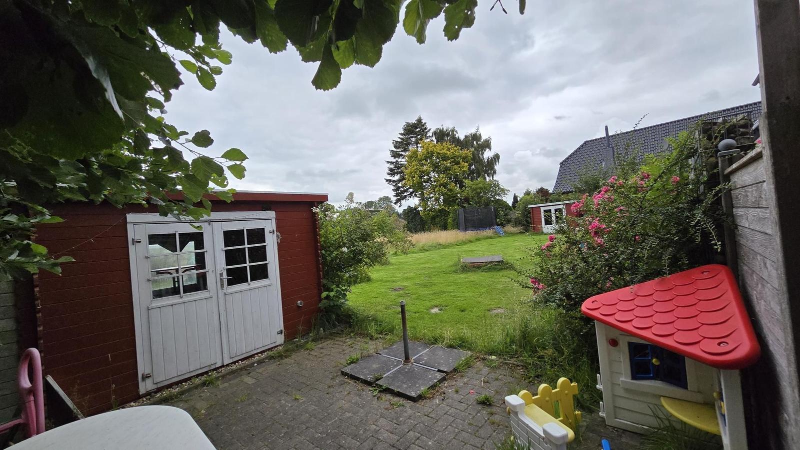 Roter Holzschuppen mit weißen Türen, Spielhaus und grüner Rasenfläche im Garten.