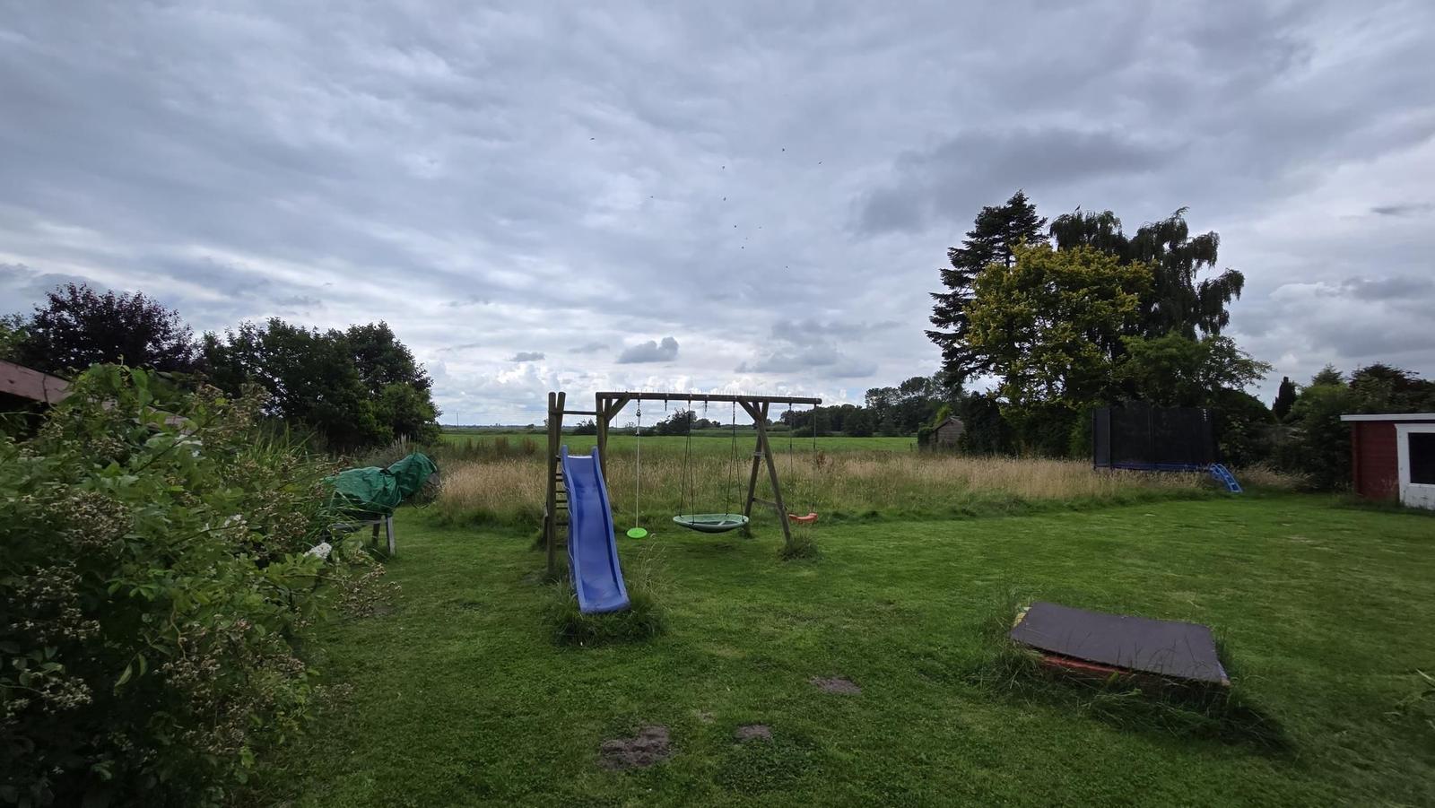 Hinterhof mit Spielplatz, Schaukel und Rutsche auf grünem Rasen.