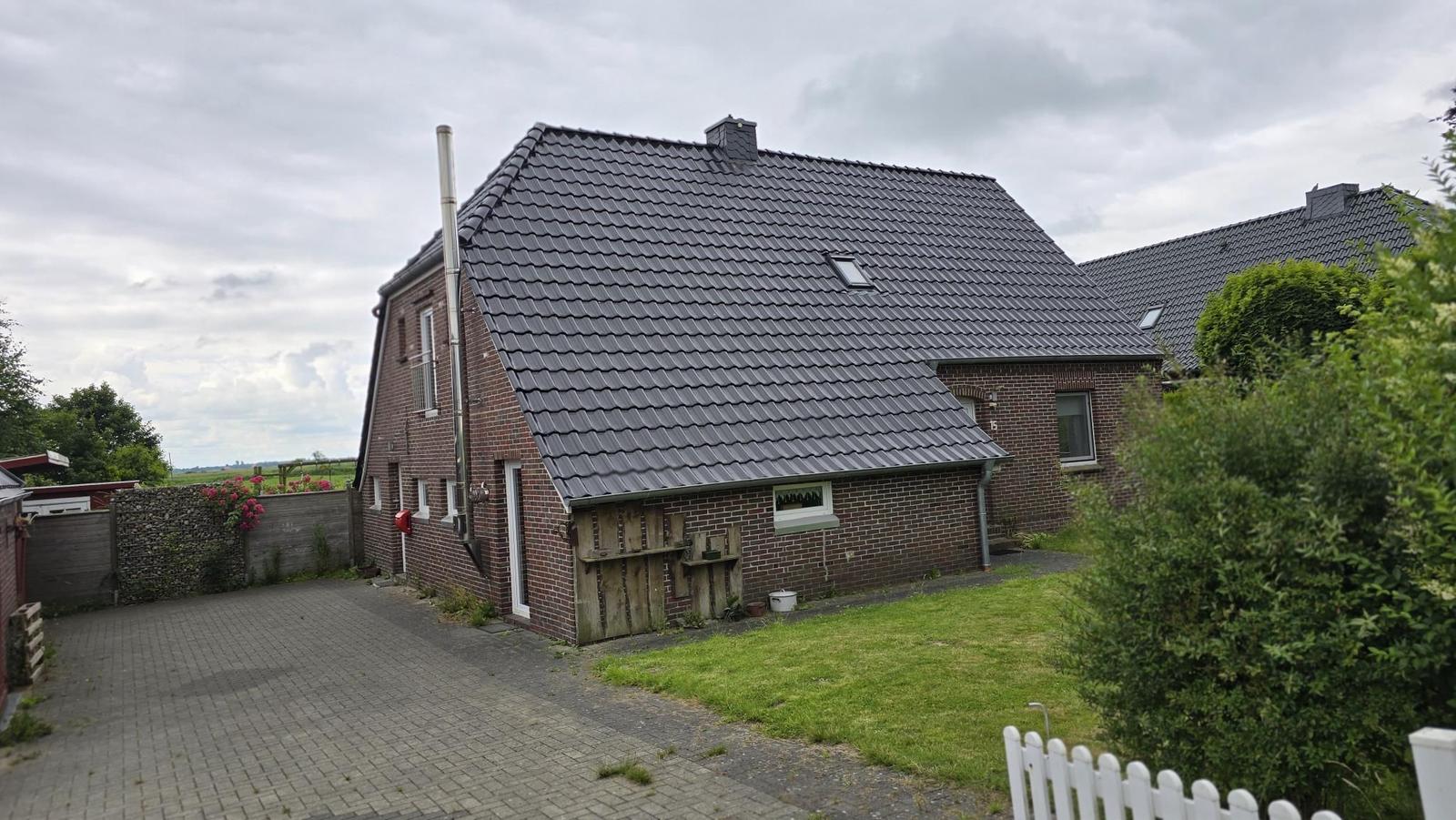 Haus mit Ziegeldach, Garten und gepflastertem Hof. 