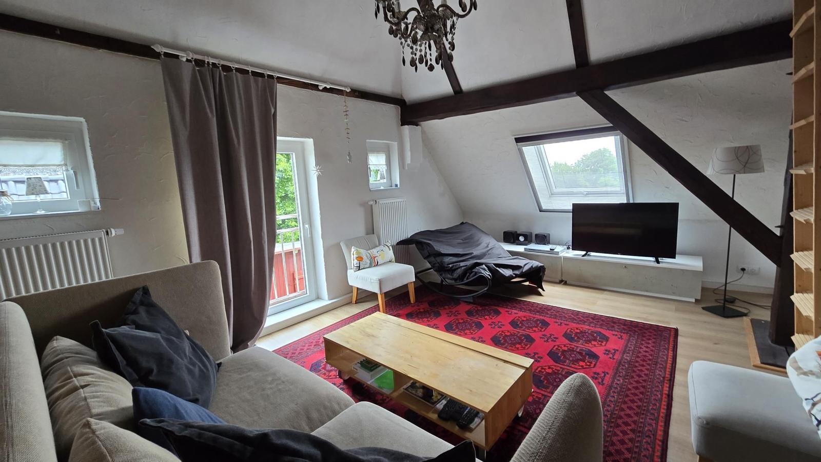 Wohnzimmer mit Sofa, Couchtisch und TV unter Holzbalkendecke.