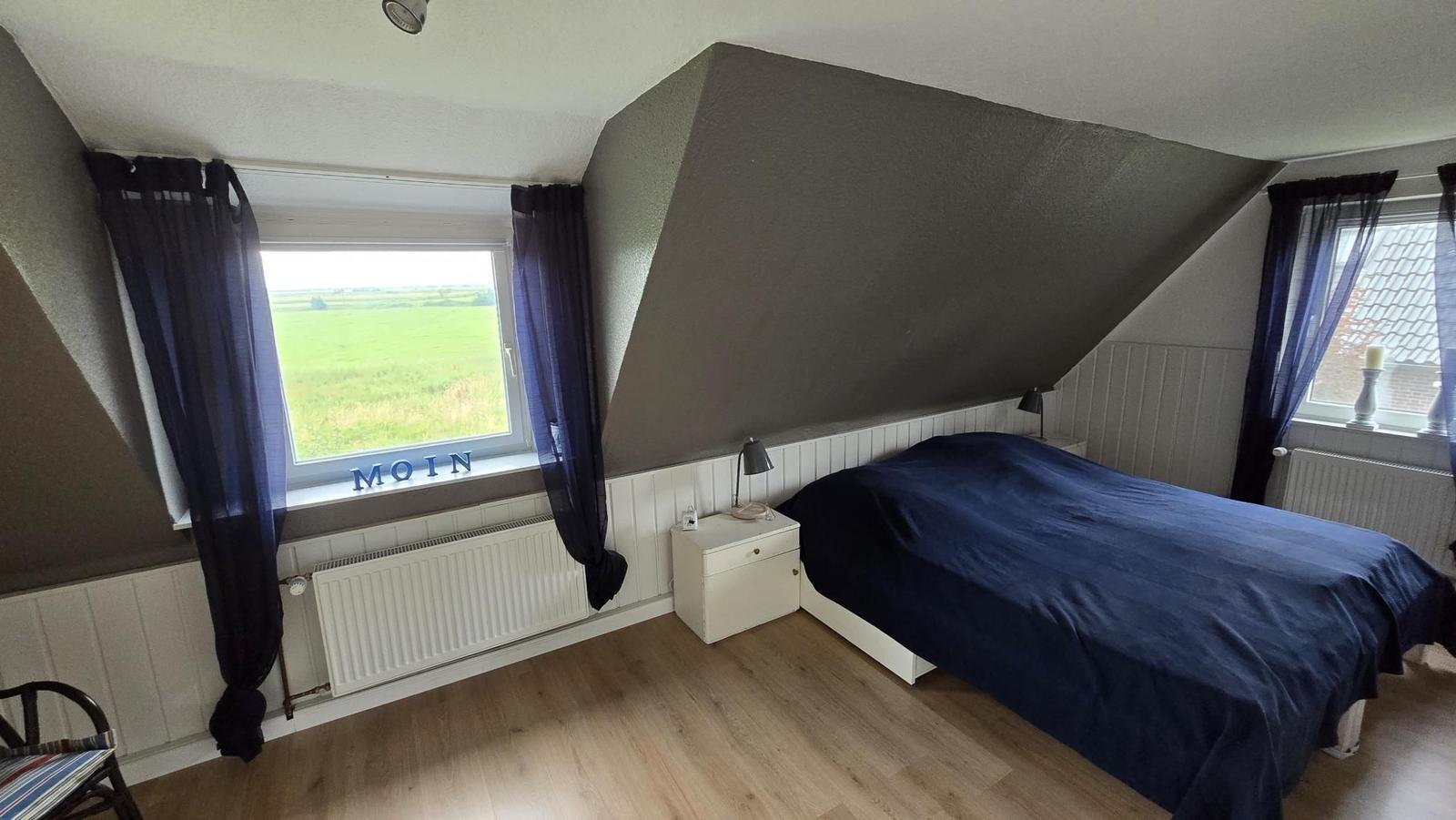 Schlafzimmer mit Dachschrägen, Bett, Fenster und Blick auf Feld.