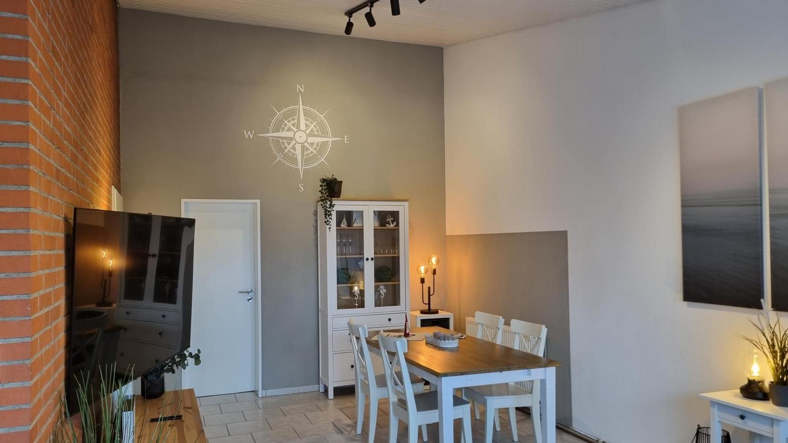 Esszimmer mit Tisch, Stühlen und Glasvitrine. Wand mit Kompassmotiv und Bild an der Wand.