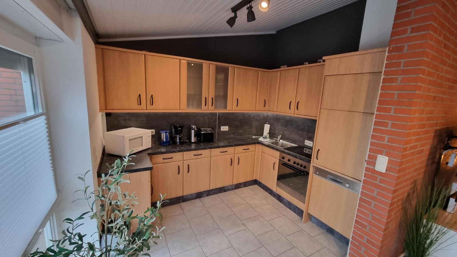 Küche mit Holzschränken, Arbeitsfläche und Fenster