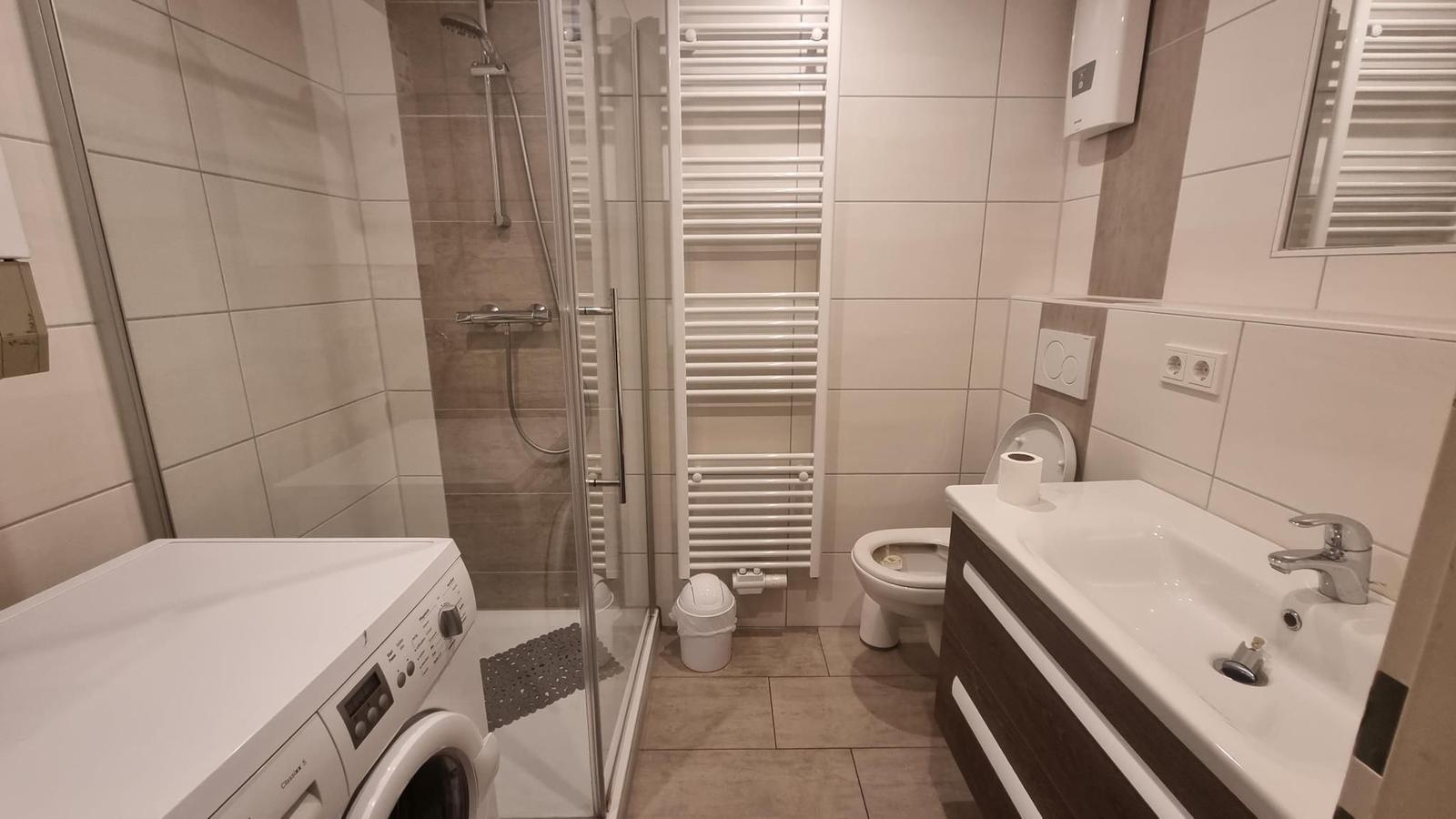 Badezimmer mit Dusche, Toilette, Waschbecken und Waschmaschine.