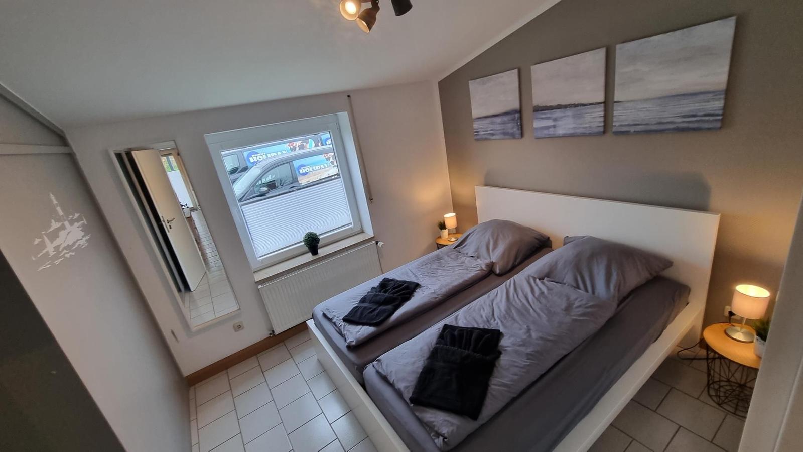 Schlafzimmer mit Doppelbett, Fenster und Wandbildern.