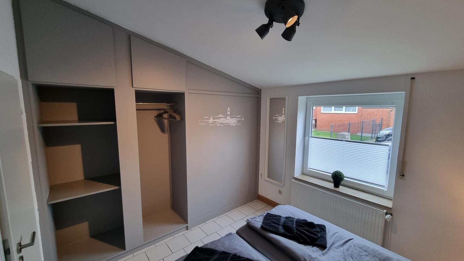 Schlafzimmer mit Kleiderschrank, Bett und Fenster mit Blick auf Außenbereich.
