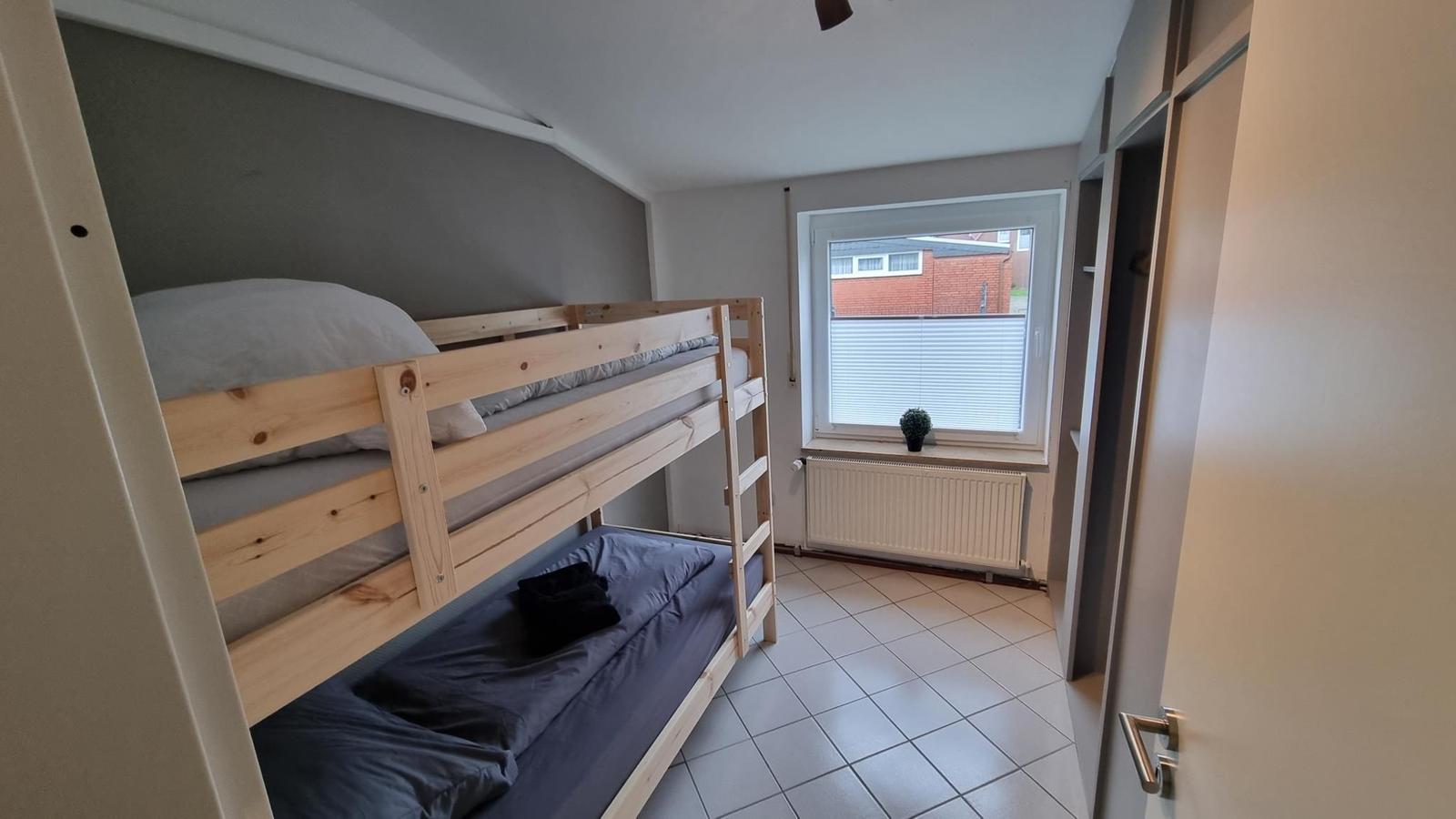 Zimmer mit Holz-Klappbett, Fenster und Heizkörper.