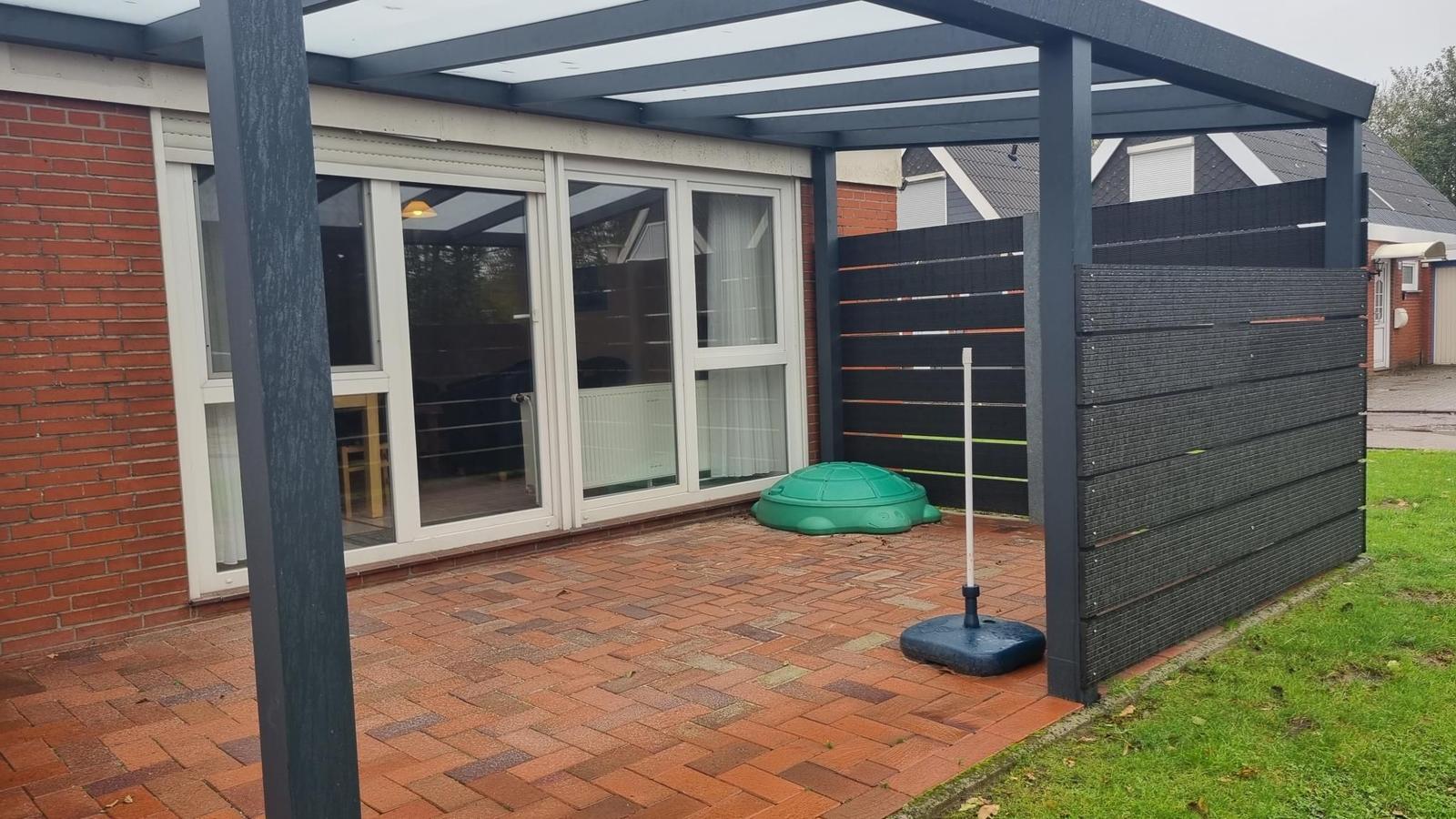 Terrasse mit Pavillon, Spielzeug und Pflastersteinen vor einem Haus mit Glasfront.
