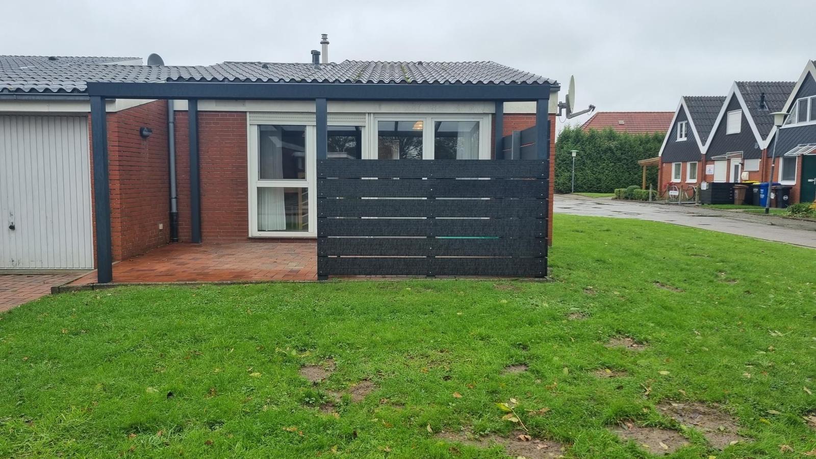 Einfamilienhaus mit Garten, Garage und Terrasse. Modernes Design mit rotem Backstein und schwarzem Zaun.