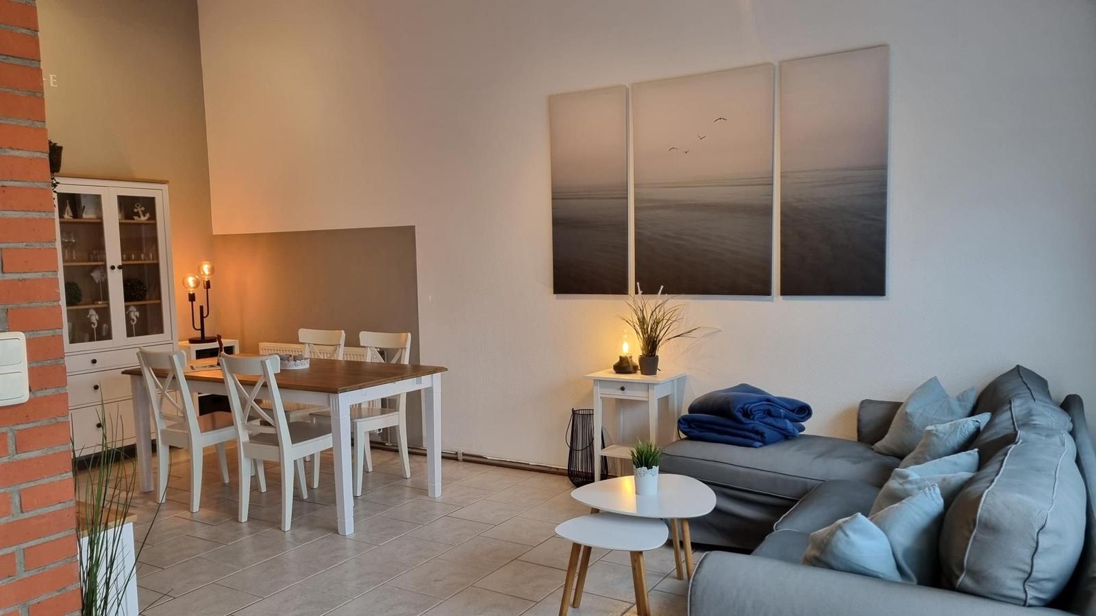 Wohn- und Essbereich mit Sofa, Tisch und Wandbildern.