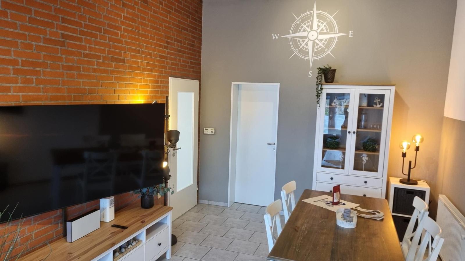 Wohn- und Essbereich mit Fernseher, Tisch und Schrank.