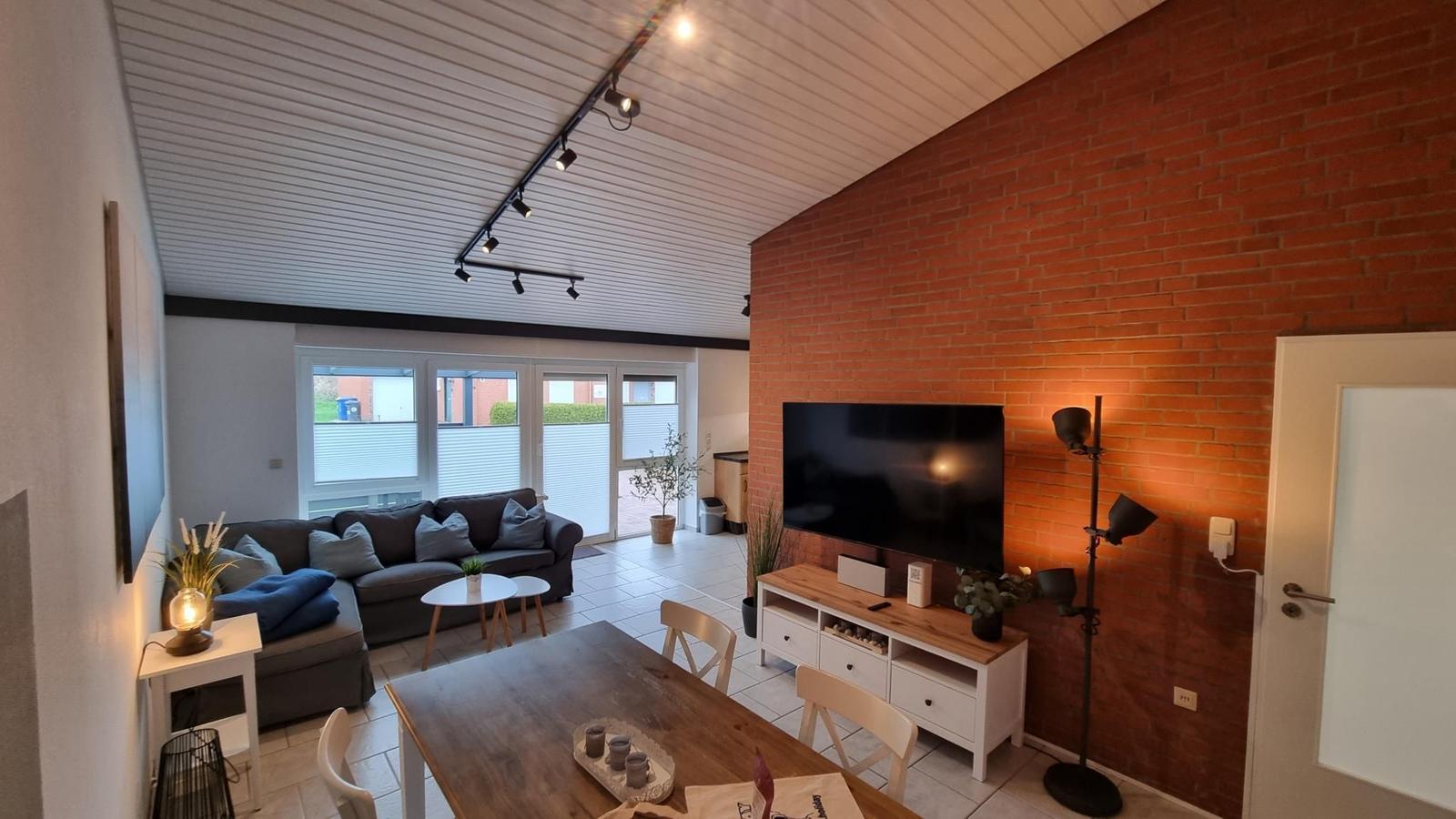 Wohn- und Essbereich mit Sofa, Fernseher und Holztisch.