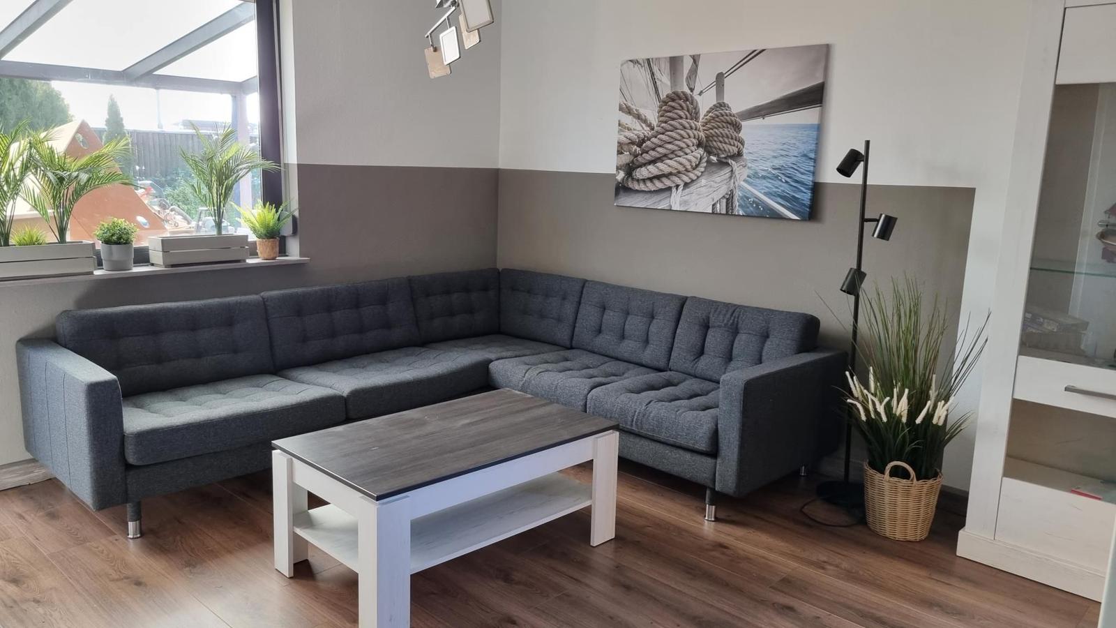 Ein Wohnzimmer mit grauem Ecksofa, Holzfußboden und Wandbild mit Seil.