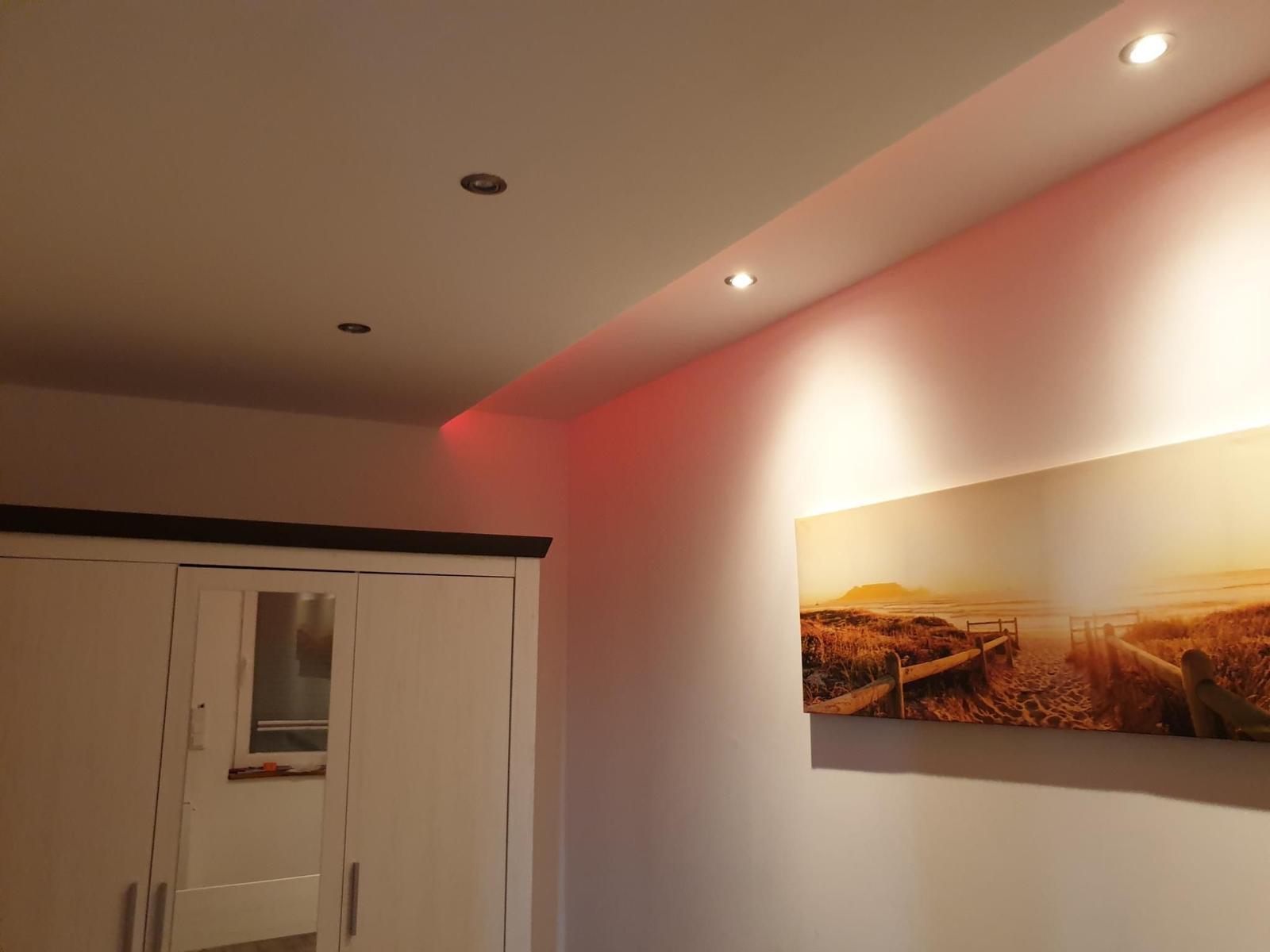 Wand mit Strandbild, weiße Schrankwand und Deckenleuchten.