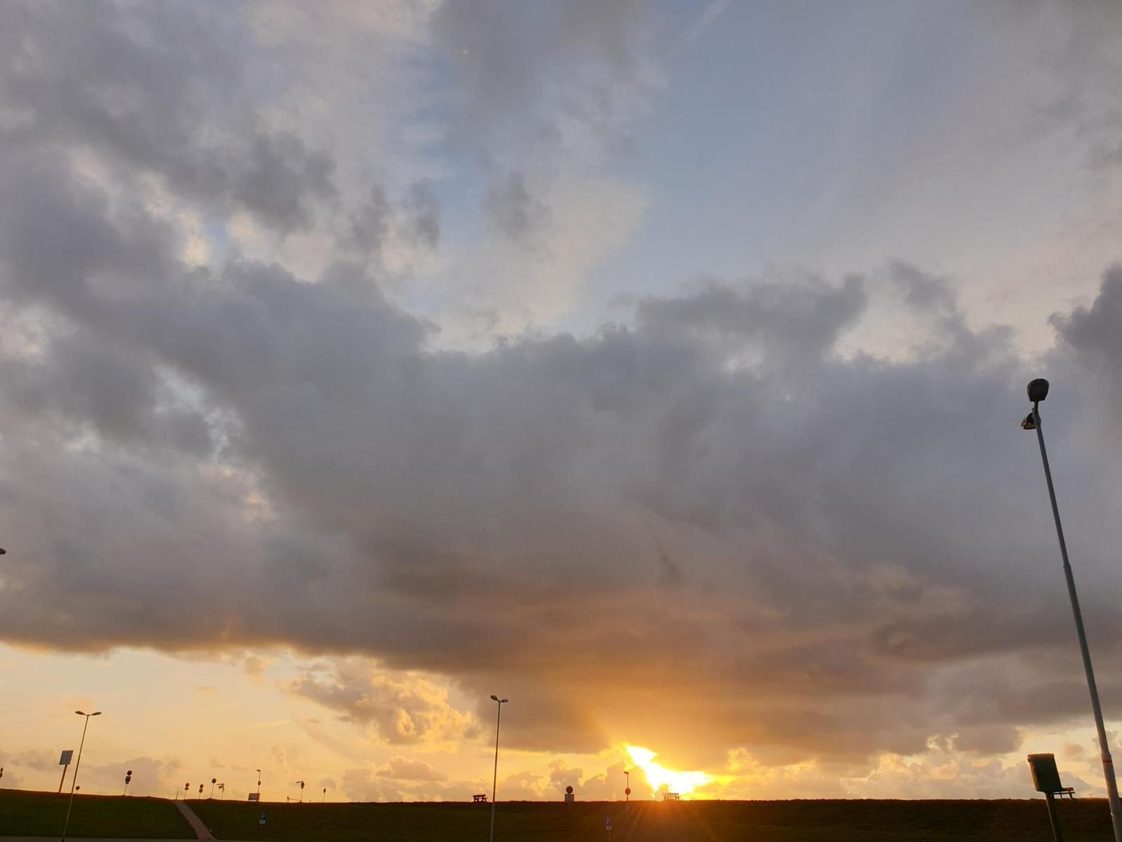 Sonnenuntergang mit dramatischen Wolken über einer grünen Fläche mit Straßenlaternen.