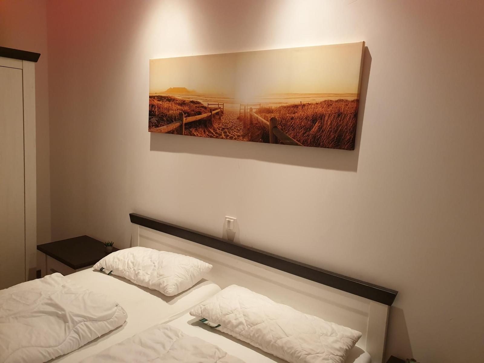 Schlafzimmer mit Bett, Wandbild und Nachttisch.