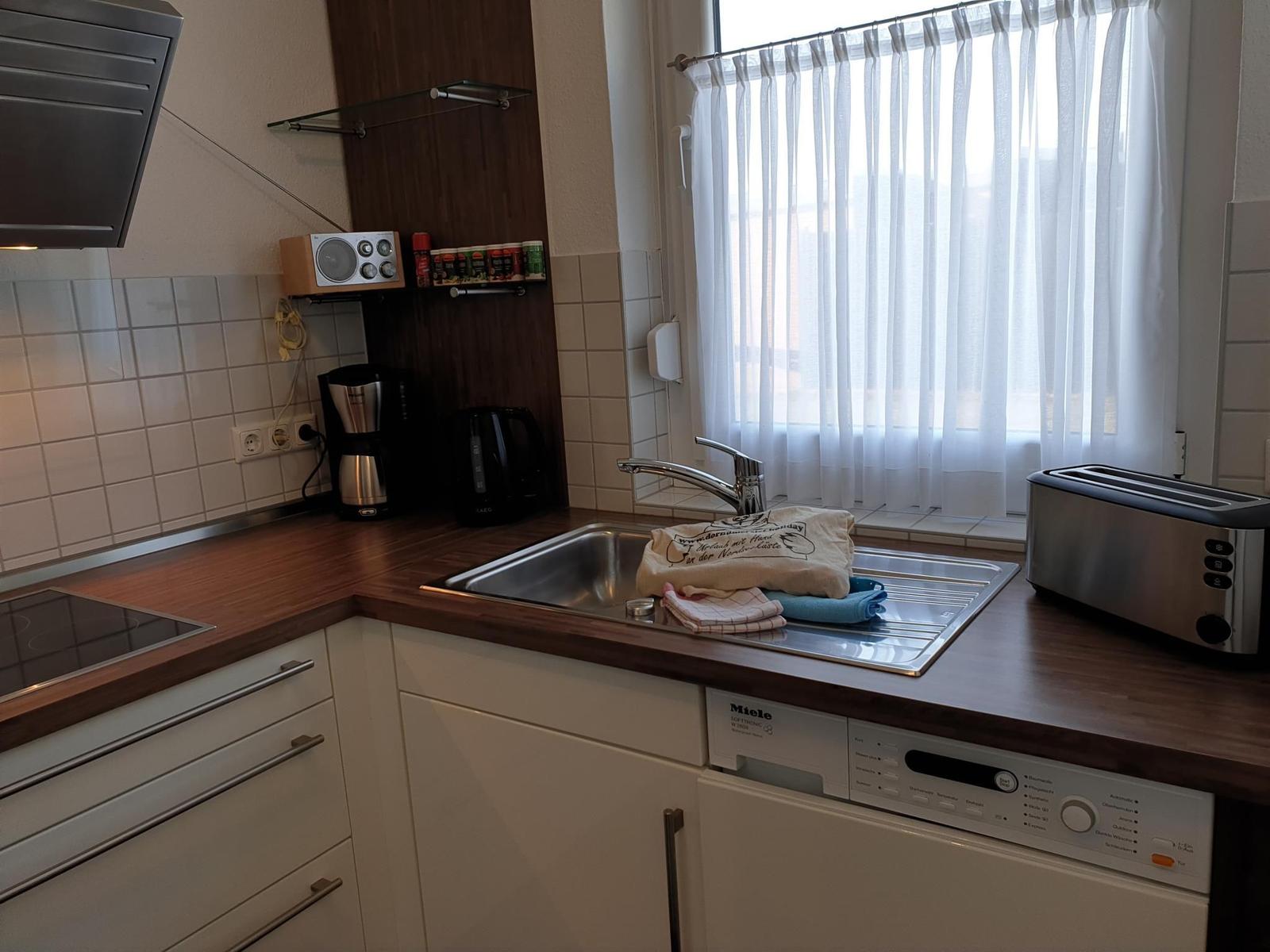 Kitchen with sink, toaster, and coffee machine next to window with white curtains.