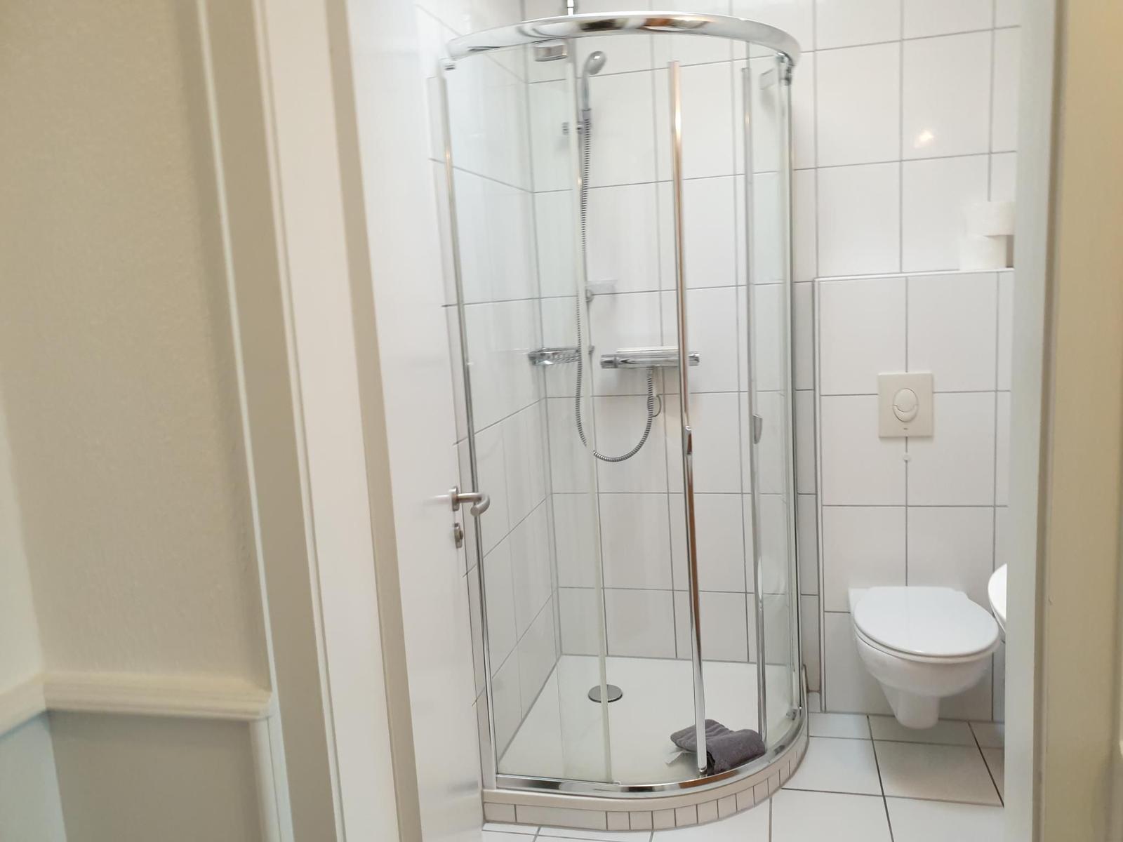Bathroom with shower, toilet, and white tiles.