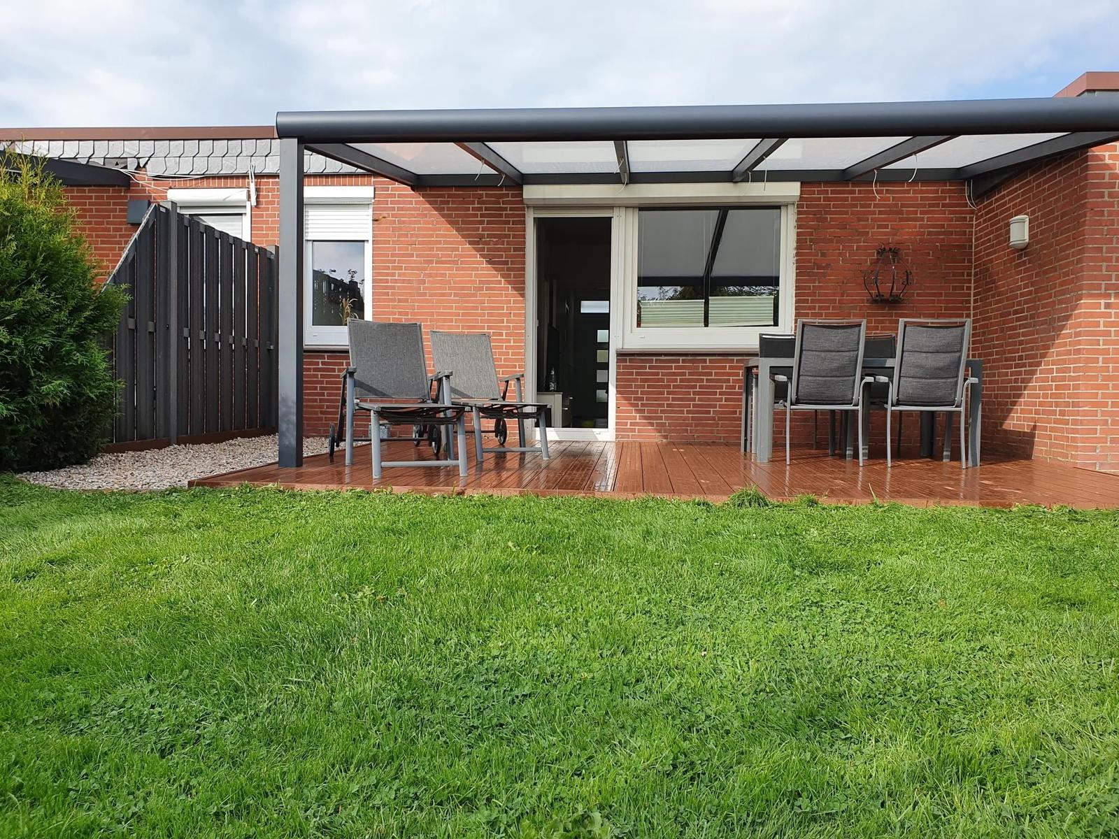 Deck with seating and garden in front of red brick house.