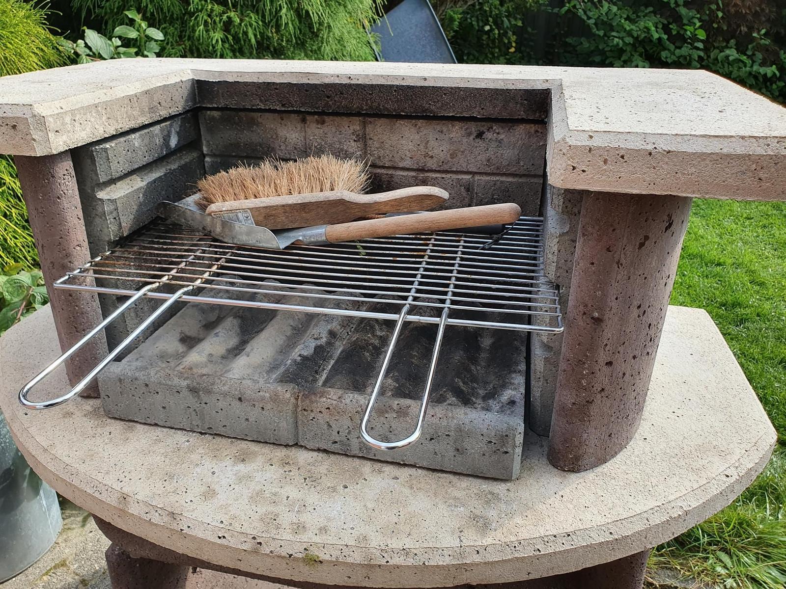 Stone barbecue with grill grate and spatula in the garden.