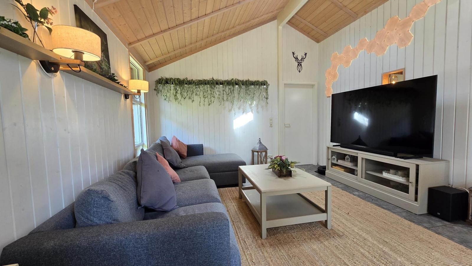 Wohnzimmer mit Sofa, Couchtisch und Fernseher. Holzdecke und weiße Wände.