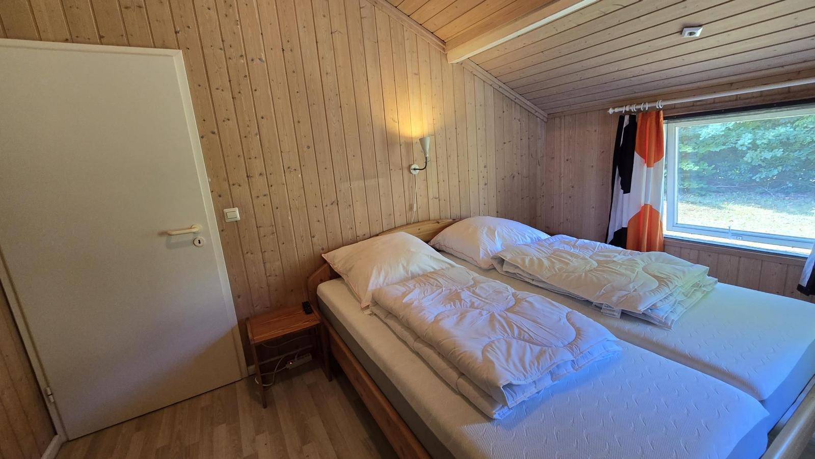 Zimmer mit Doppelbett, Holzwand und Fenster zum Wald