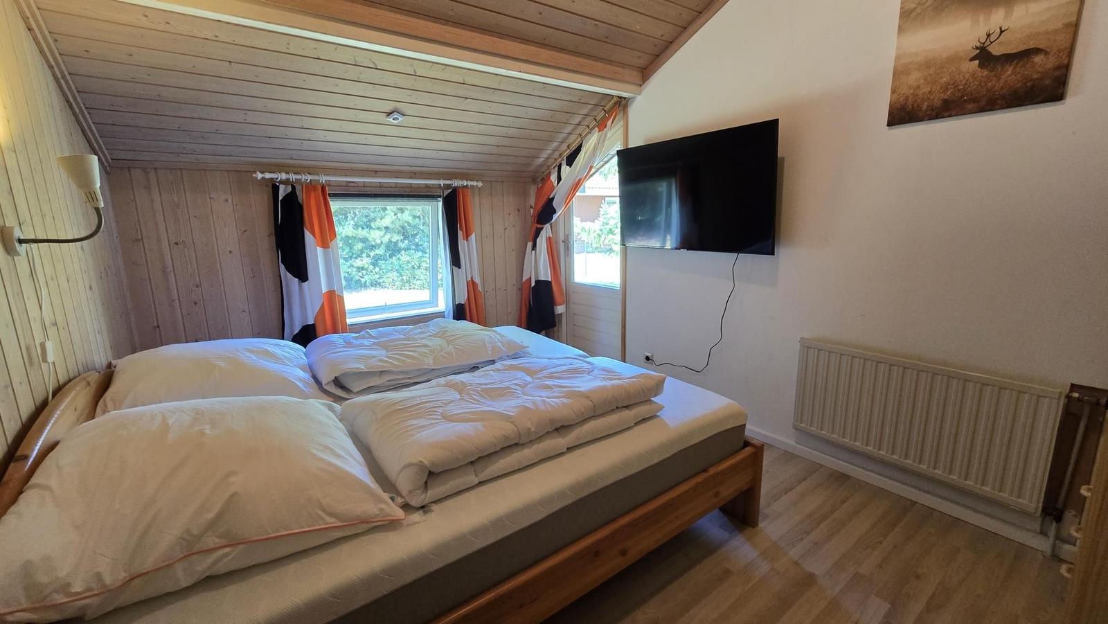 Schlafzimmer mit Bett, TV und Fenster mit Blick auf Grün.