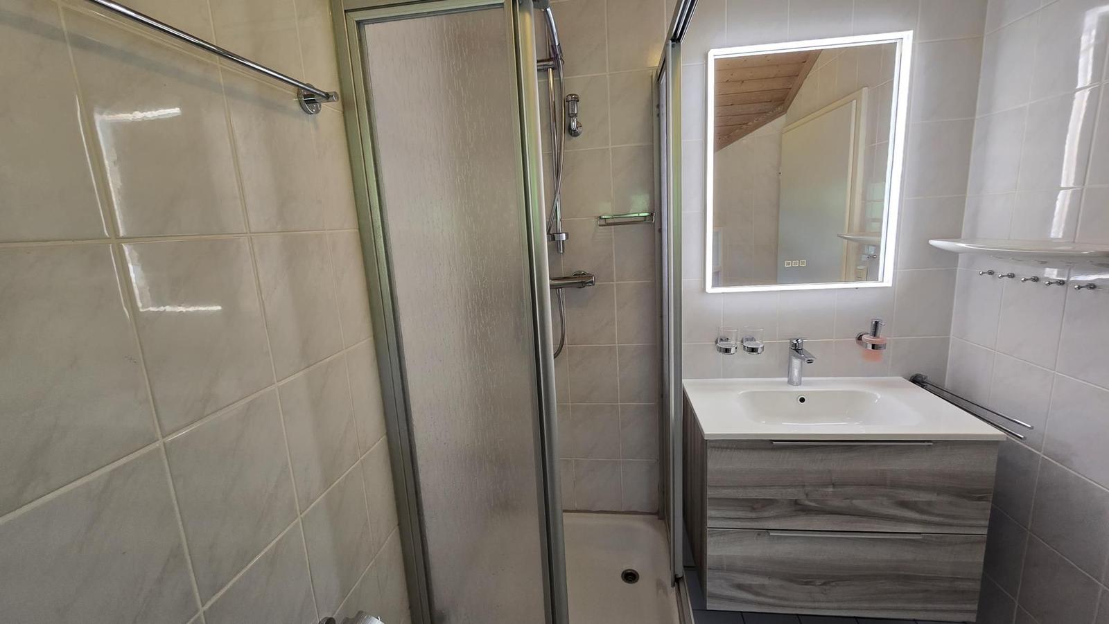 Badezimmer mit Dusche, Waschbecken und beleuchtetem Spiegel.