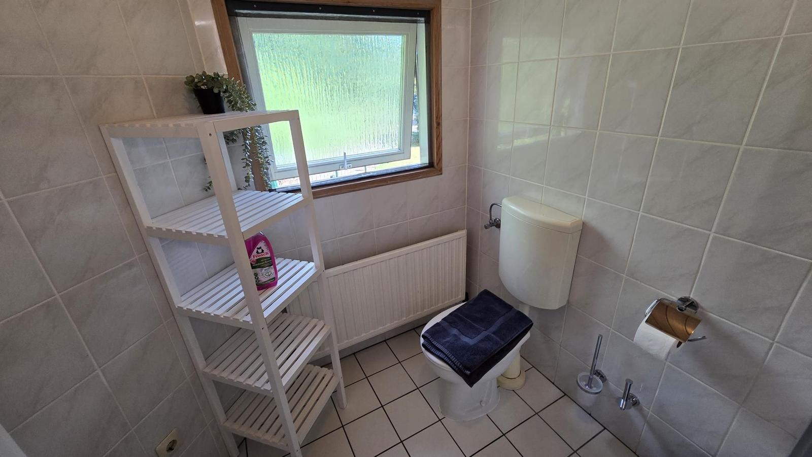 Badezimmer mit Toilette, Fenster und weißen Fliesen.