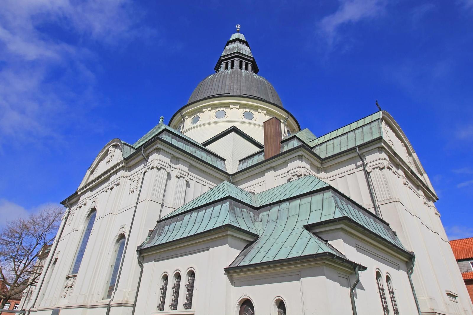 Weißes Kirchengebäude mit kupferfarbenem Dach und Kuppel unter blauem Himmel.