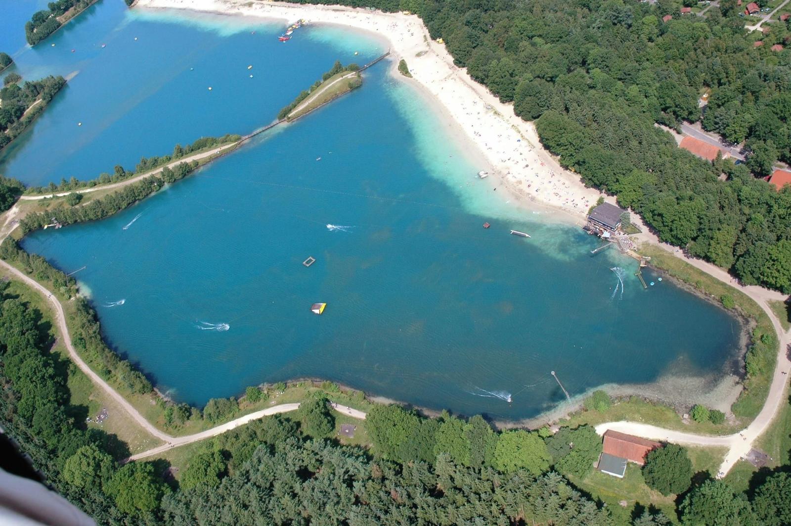 Aerielansicht eines Sees mit Strand, Booten und Waldumgebung.