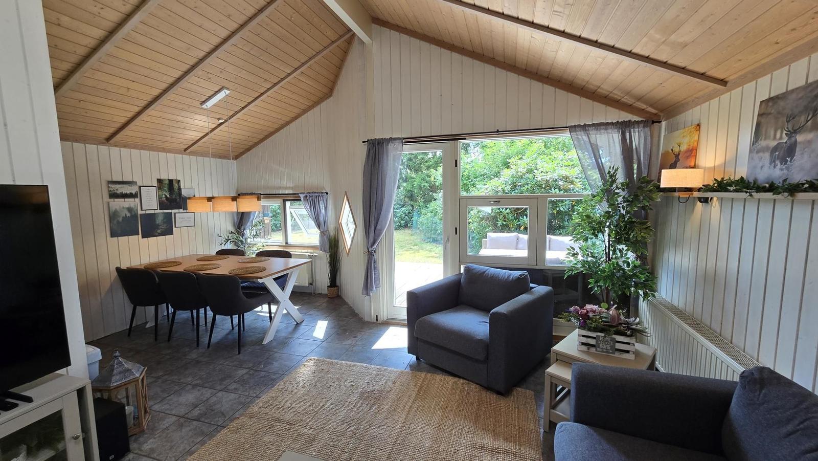 Wohn- und Essbereich mit Sitzgelegenheiten, Tisch, TV und Blick auf den Garten.