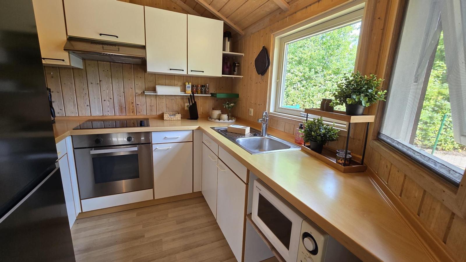 Küche mit Holzwand, Spüle, Herd und Fenster mit Blick auf Grün.
