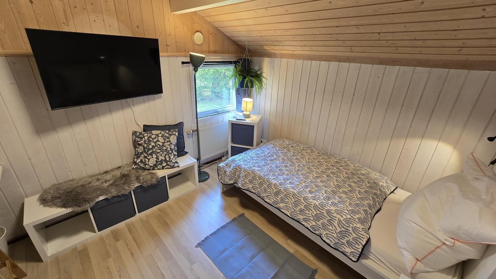 Schlafzimmer mit Bett, Fernseher und Fenster.