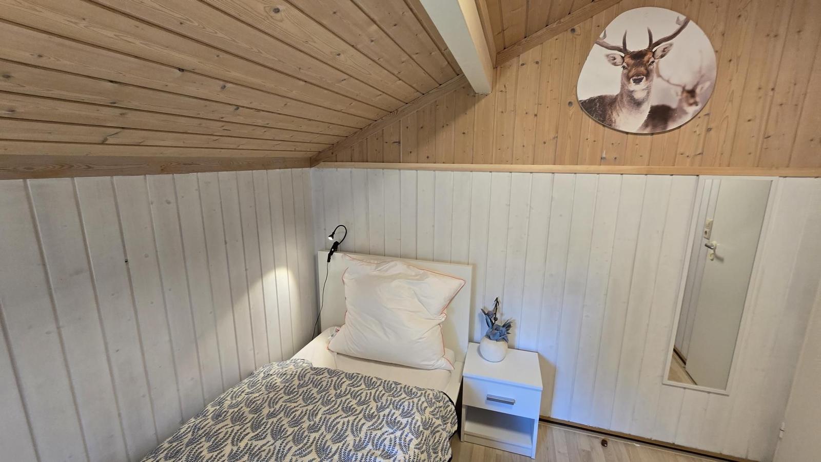 Schlafzimmer mit Bett, Nachttisch und Wandbild von Hirsch.