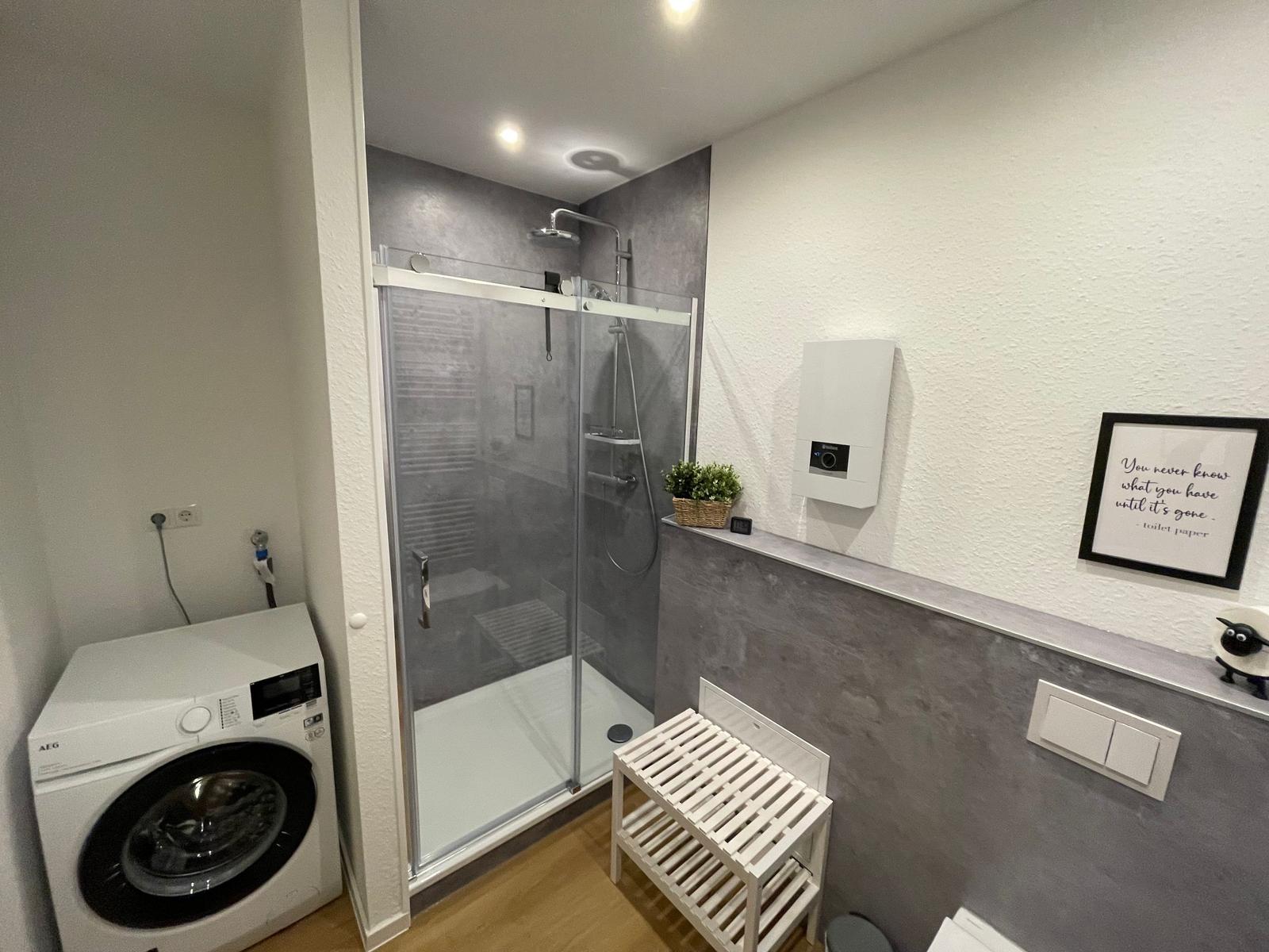 Badezimmer mit Dusche, Waschmaschine und Holzboden.