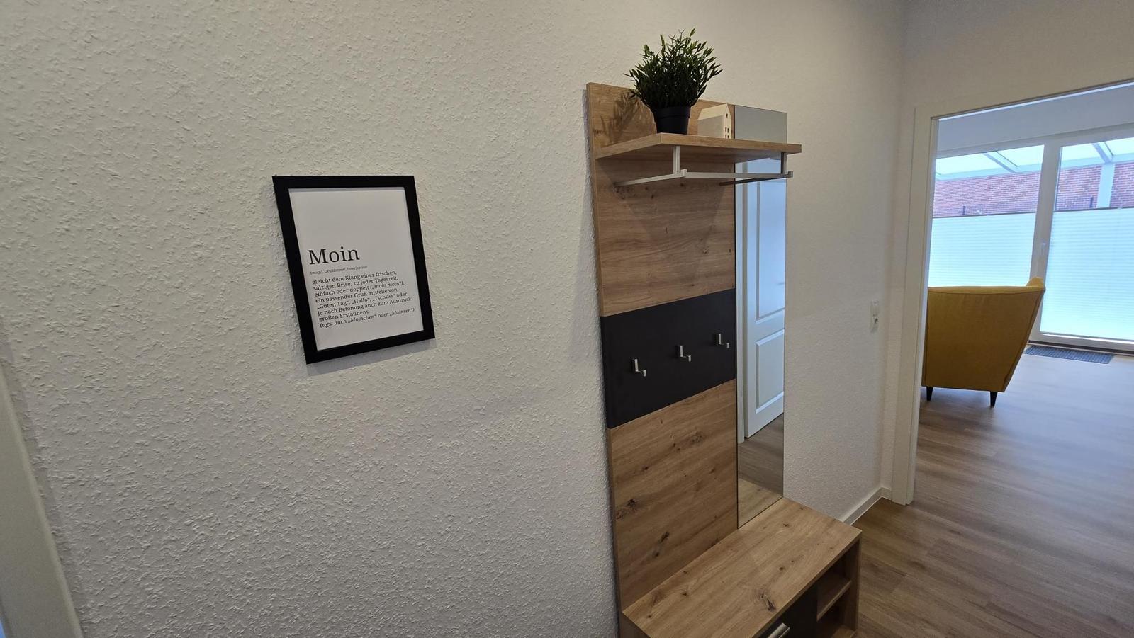 Eingangsbereich mit Garderobe, Wandbild und Blick in Wohnzimmer.