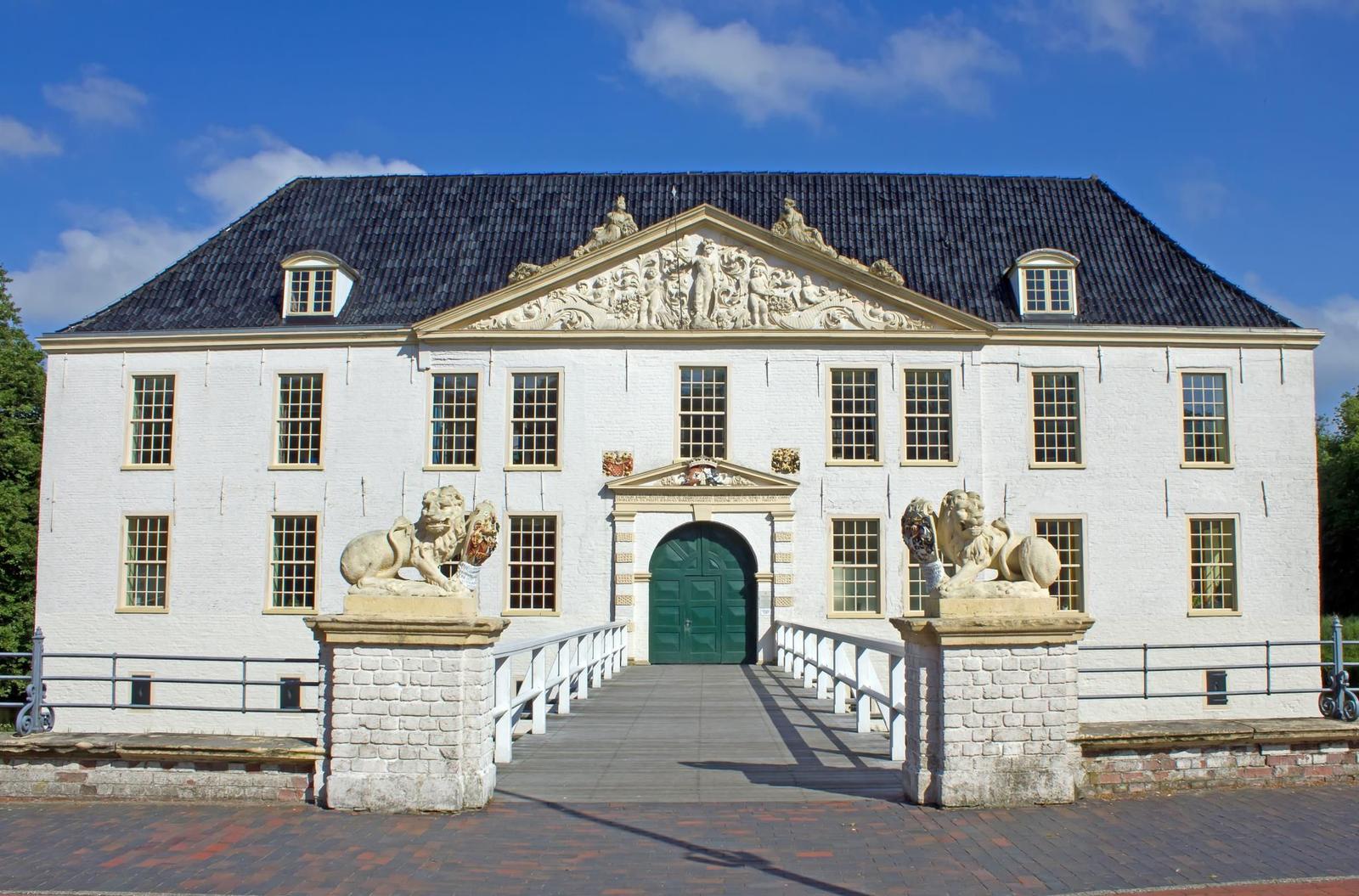 Weiße Villa mit dunklem Dach und grüner Tür. Zwei Löwenstatuen flankieren den Eingang.