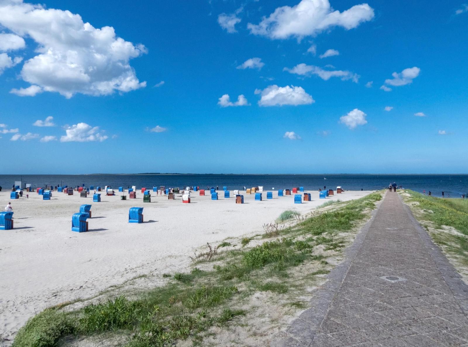Strand mit bunten Liegestühlen und Promenade unter blauem Himmel.