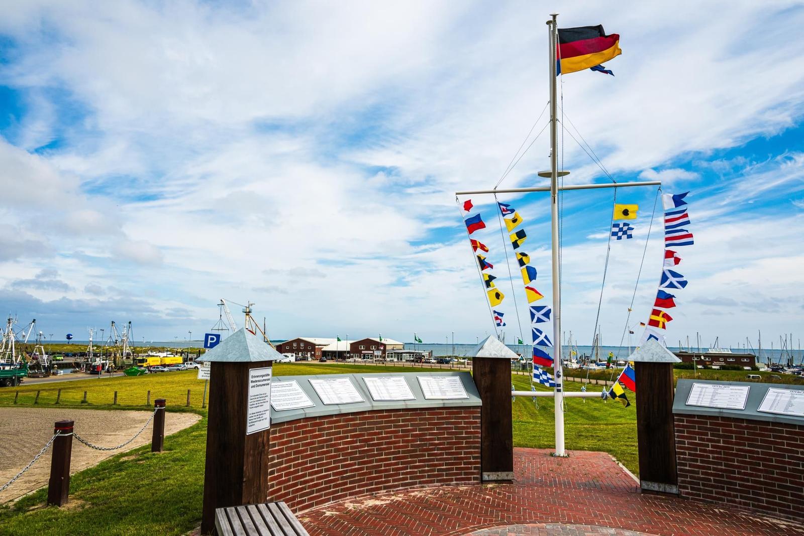 Marineflaggenmast mit deutscher Flagge und Informationsplaketten im Hafenbereich.