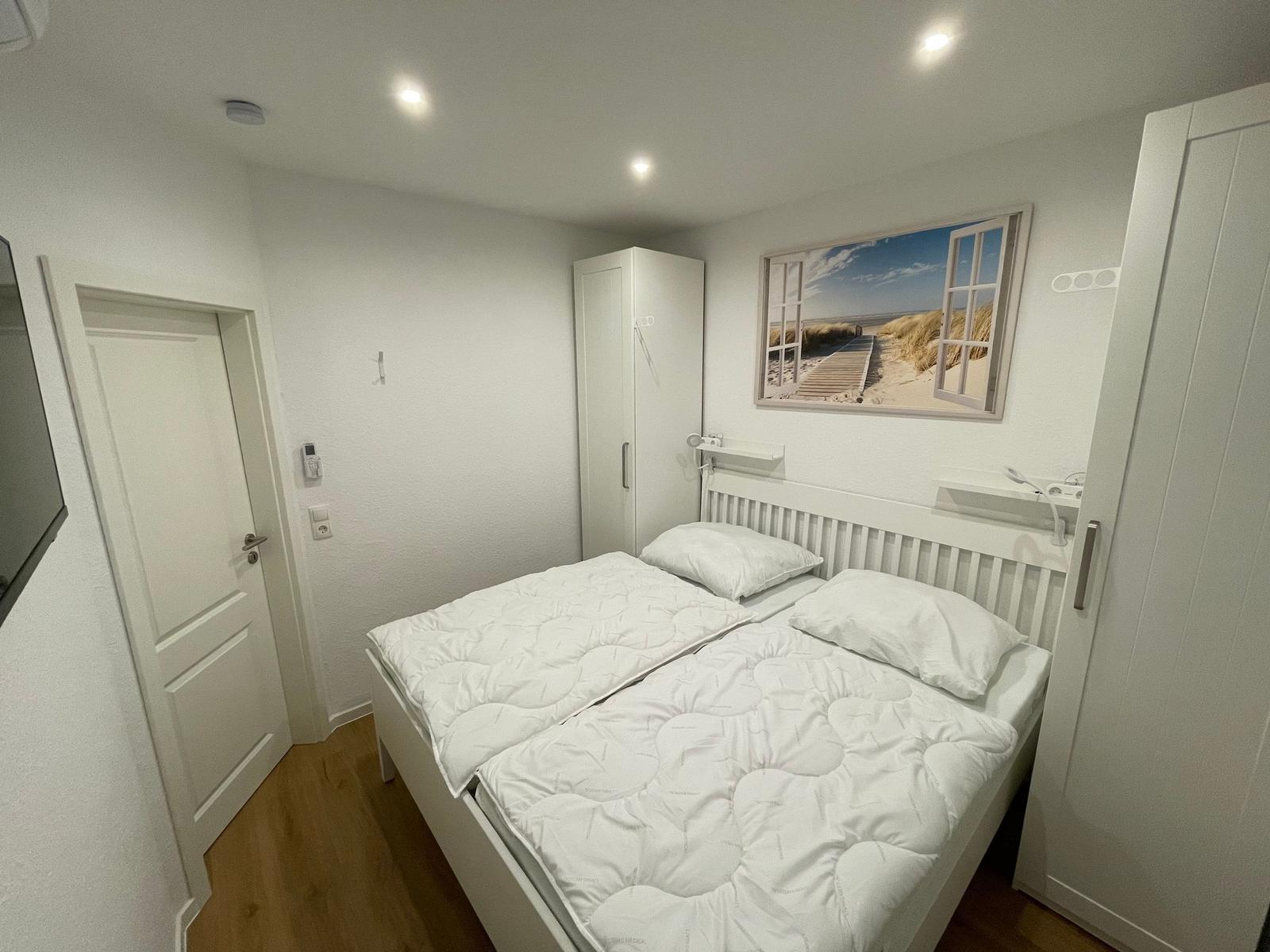 Schlafzimmer mit Doppelbett, weißen Möbeln und Wandbild.