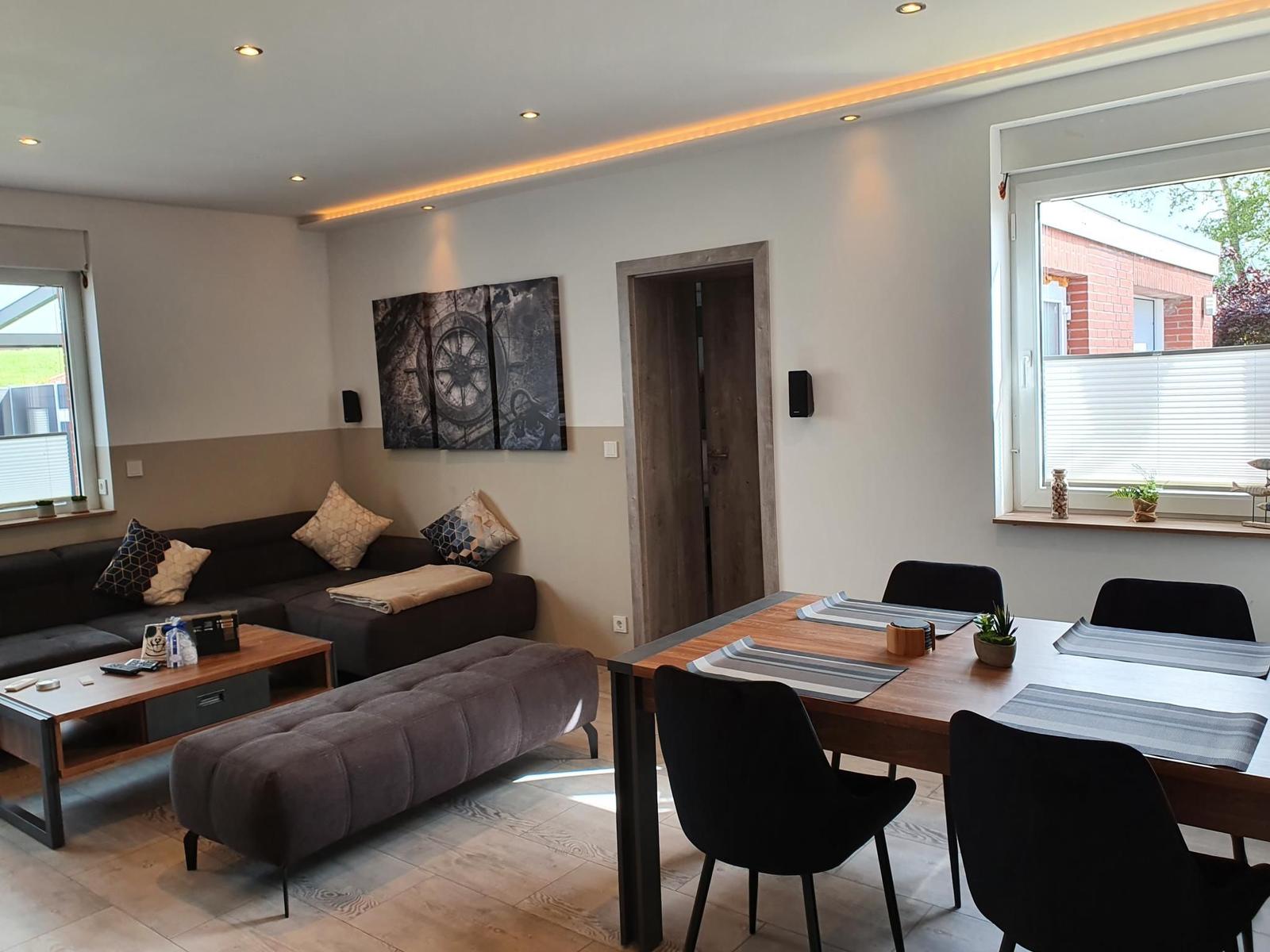 Wohn- und Essbereich mit Sofa, Tisch und Stühlen. Wandbild und Fenster sichtbar.